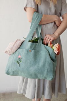 a woman holding a green bag with flowers on the inside and side pockets that have been embroidered onto it