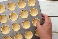 a person holding a pan filled with cupcakes on top of a wooden table