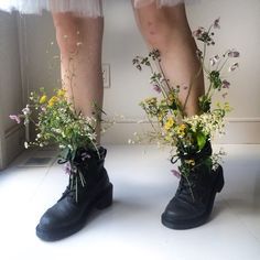 two pairs of legs wearing boots with flowers in them and one pair is standing on the floor