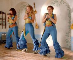 three women in blue and gold outfits are dancing on the dance floor with their instruments