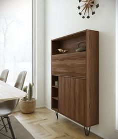 a wooden cabinet sitting in front of a window next to a table with chairs and a clock on the wall