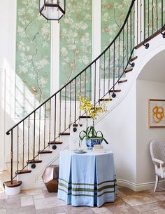 there is a table with flowers on it in front of the stair case and wall paper