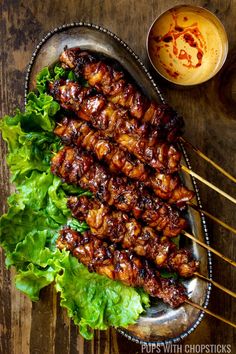 several skewers of meat and lettuce on a metal plate with dipping sauce