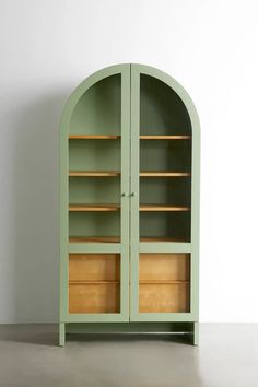 a green bookcase with two doors and shelves on the top, in front of a white wall