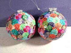 two christmas balls with different colored buttons on them sitting next to each other in front of a purple wall