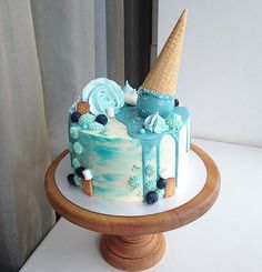 a blue and white cake with an ice cream cone on top is sitting on a wooden stand