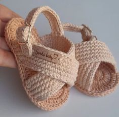 a hand holding a crocheted baby sandal with a name tag on it