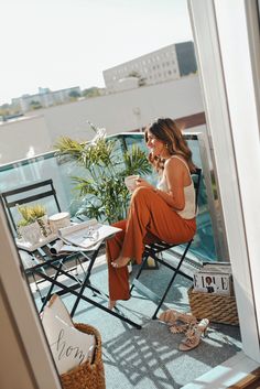 a woman sitting at a table on top of a balcony next to a window looking out