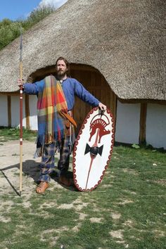 a man standing in front of a thatched roof house holding a spear and shield