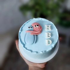 a hand holding a blue cake with an octopus on it