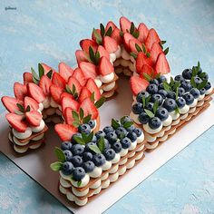 a number made out of cookies with strawberries and blueberries on top, sitting on a table