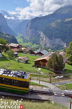 a yellow and green train traveling through a lush green valley filled with mountains in the background