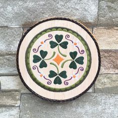 a round wooden plaque with four leaf clovers on it's side, mounted on a stone wall