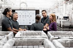 some people are standing around in a factory and looking at something on the wall behind them