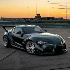 a black sports car parked on top of an airport tarmac with the sun setting in the background