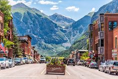 cars are parked on the street in front of buildings with mountains in the back ground