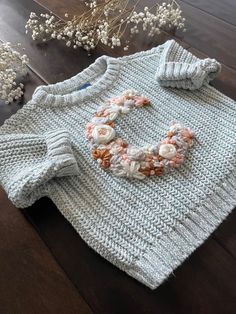 a knitted sweater with flowers on the collar and sleeves, sitting on a wooden table