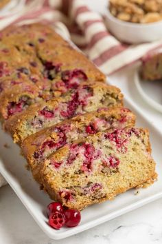 a loaf of cranberry bread sitting on top of a white plate with cherries