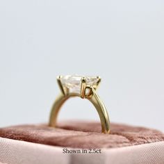 a gold ring with a white diamond in it sitting on top of a pink cloth