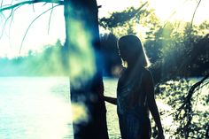 a woman standing next to a tree near the water