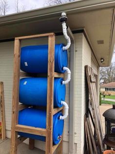 a ladder is holding three large blue barrels on the side of a house, with pipes running from it