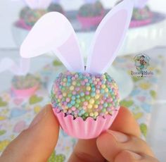 a hand holding a cupcake with sprinkles and bunny ears on it