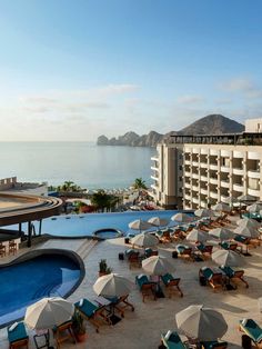 an outdoor swimming pool with umbrellas and chaise lounge chairs next to the ocean