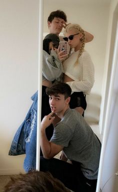 a man taking a selfie in front of a mirror with two women behind him