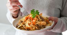 a woman is holding a plate of food with carrots, cabbage and meat on it