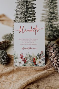 a white card with red writing on it sitting next to pine cones and evergreens