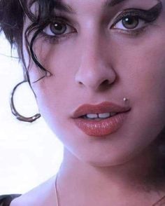 a close up of a woman with piercings on her nose and eyes, looking at the camera