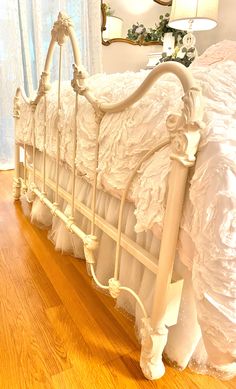 a white bed with ruffled bedspread and wooden floors