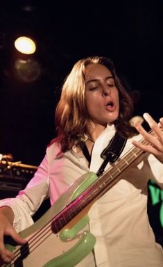 a woman holding a bass in her right hand and singing into a microphone on stage