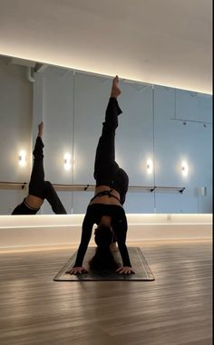 two people doing yoga poses in an empty room with mirrors on the wall behind them