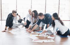 a group of people sitting on the floor looking at papers and pencils - stock photo - images