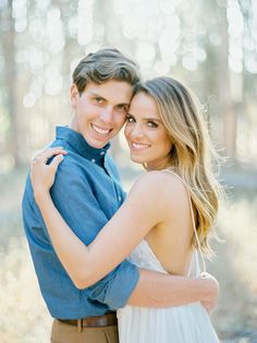 a young man and woman embracing each other in front of some trees with sunlight shining on them