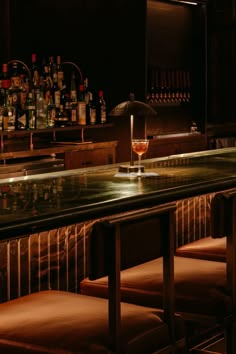 a dimly lit bar with stools and bottles in the background