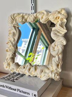 a mirror sitting on top of a table next to a book and plant in front of it