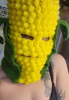 a woman wearing a yellow crocheted corn on the cob mask and black harness