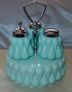 two blue glass pots on top of a white cake stand with silver handles and knobs