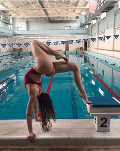 a woman in a red swimsuit doing a handstand on a diving board