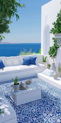 an outdoor living room with white furniture and blue tiles on the floor, overlooking the ocean