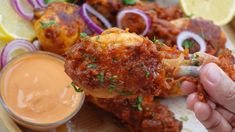 a person is dipping sauce on chicken wings with lemons, onions and red onion