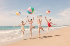 four women in bathing suits are playing with beach balls on the beach