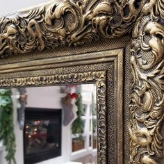 an ornate gold framed mirror in front of a fireplace with christmas decorations on the mantel