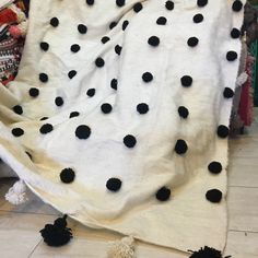 a white blanket with black polka dots and pom poms on the floor next to a pile of stuffed animals