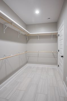 an empty walk in closet with white walls and wooden rails on the wall, along with light wood flooring