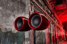 two red speakers sitting on top of a metal pole in front of a brick wall