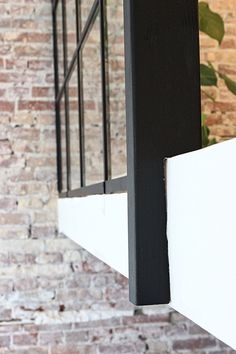 an open window on the side of a brick wall next to a planter with green leaves