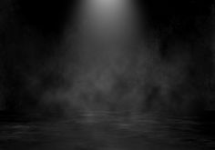 an empty dark room with light coming from the ceiling and fog on the floor in front of it